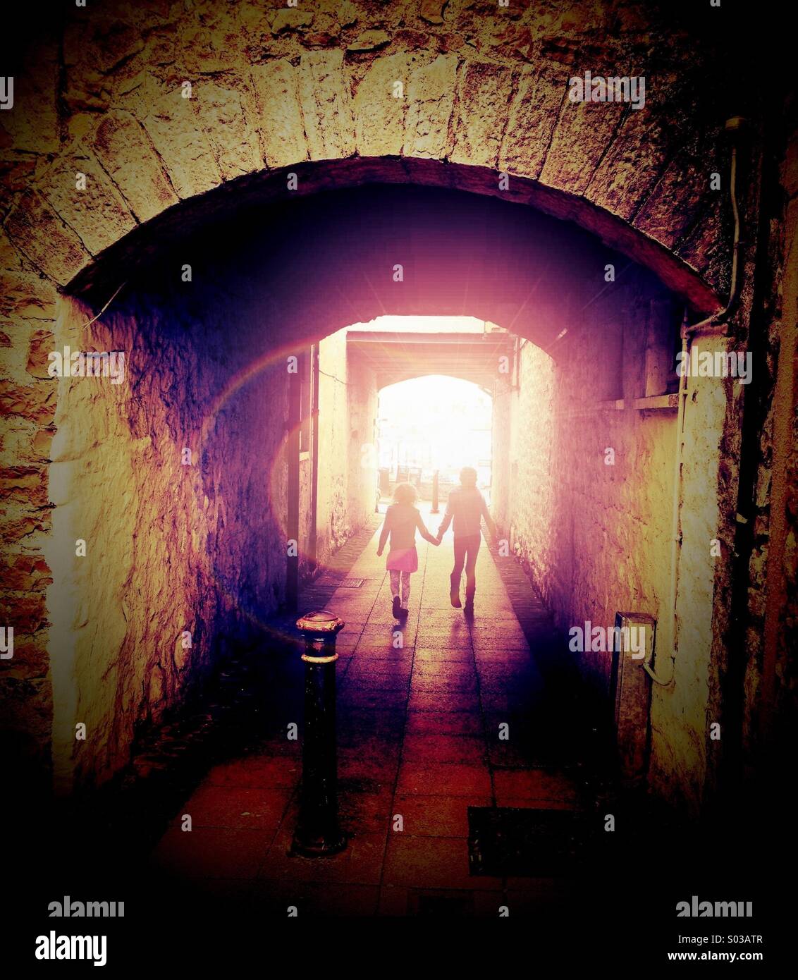 Due figli che camminano mano nella mano lungo il passaggio verso la luce Foto Stock