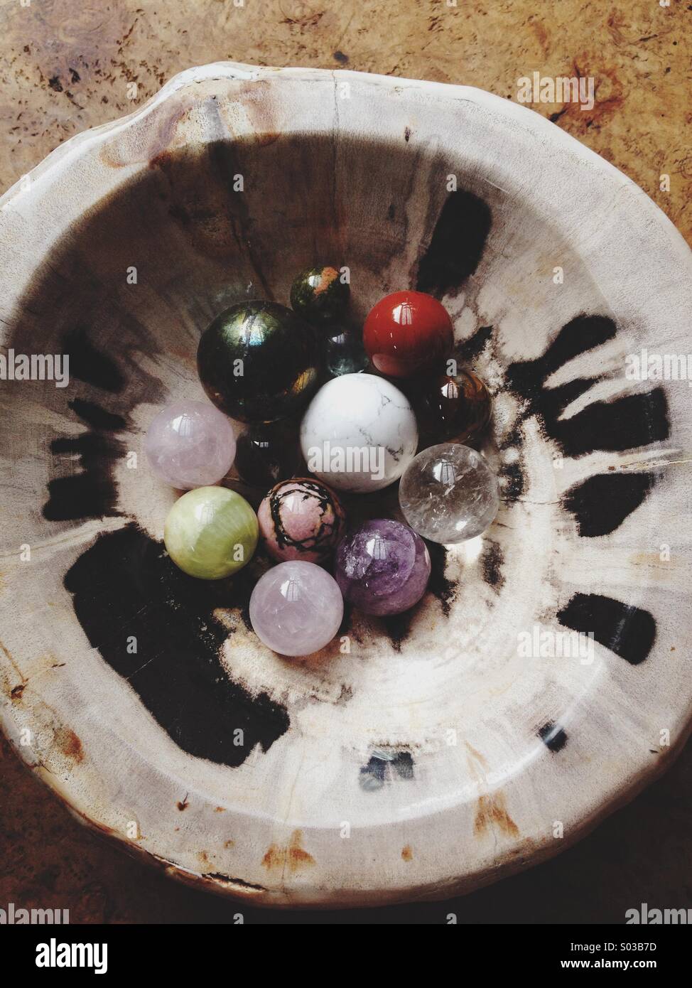Più lucido cristallo multicolore e sfere di pietra in legno pietrificato ciotola sul tavolo rustico. Foto Stock