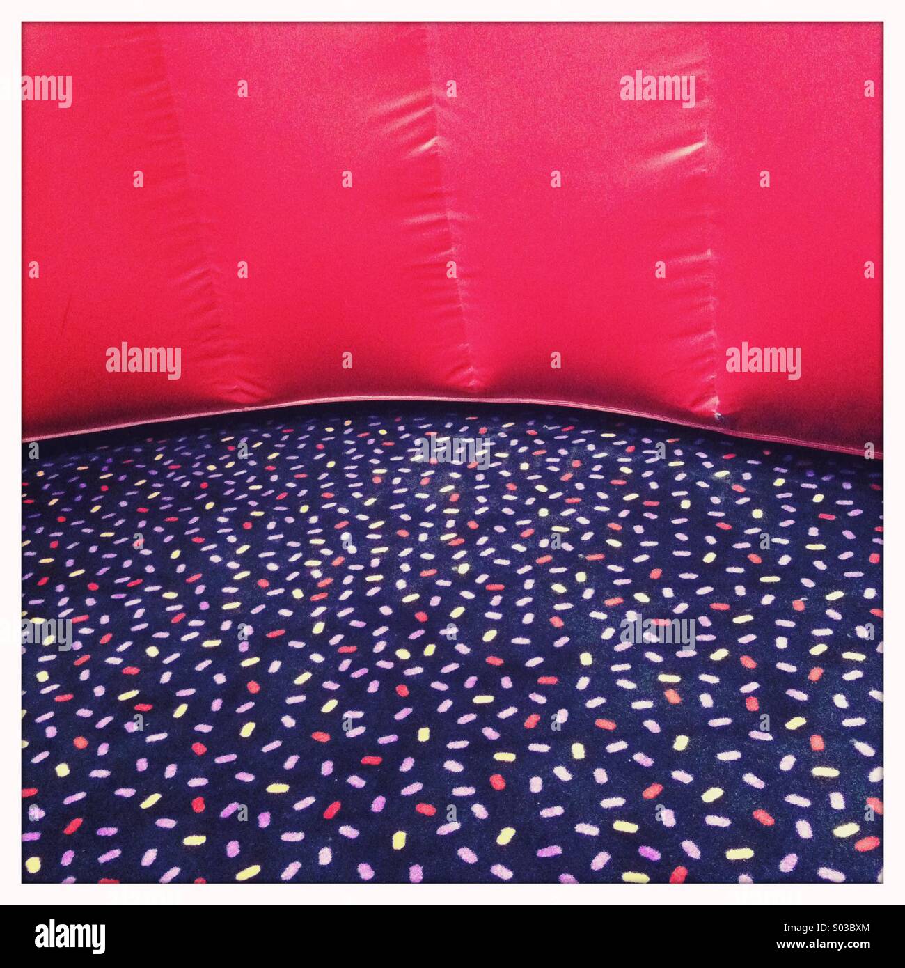 Un coloratissimo tappeto a motivi geometrici con una luminosa parete rossa Foto Stock