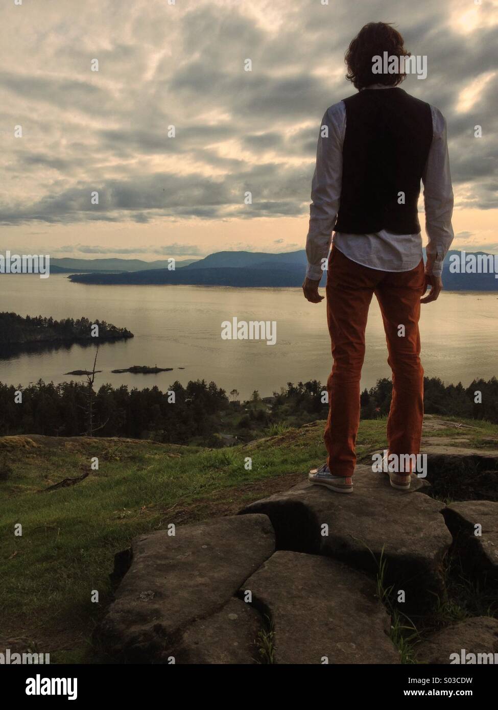 Ben vestito uomo in piedi sulla parte superiore di alta collina con vista sull'oceano/acqua e isole. Foto Stock