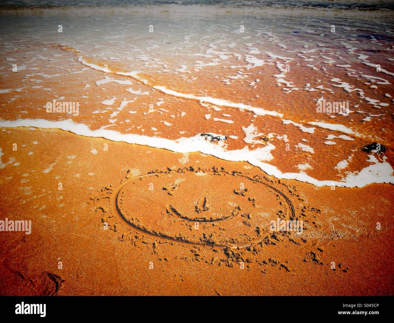 Smiley face in sabbia in procinto di essere lavati via dalla marea Foto Stock