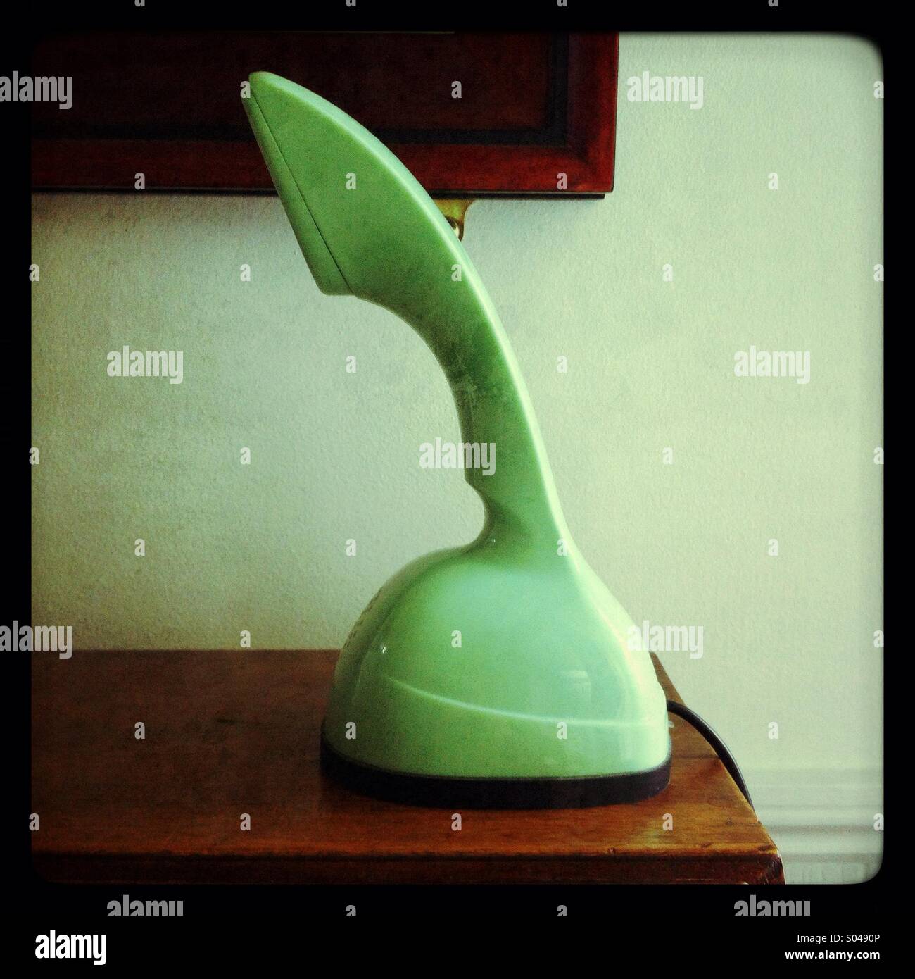 Lampada da scrivania verde vintage accanto a mobili in legno in un ambiente interno accogliente - Immagine stock catturata con smartphone