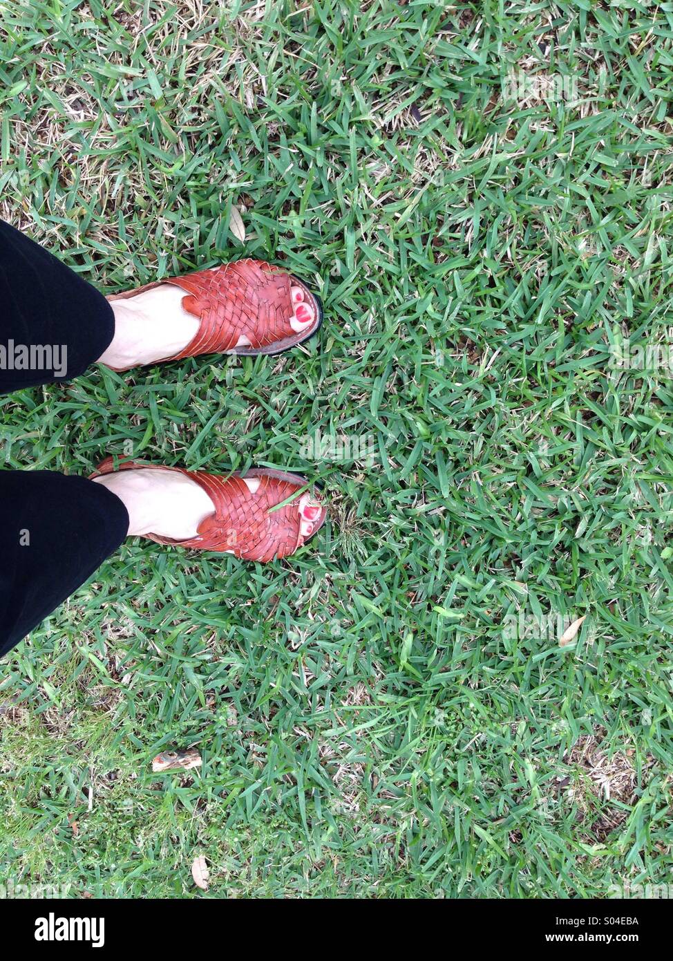 In piedi in erba, che indossa pantaloni neri e sandali huarache, con puntale rosso chiodi Foto Stock