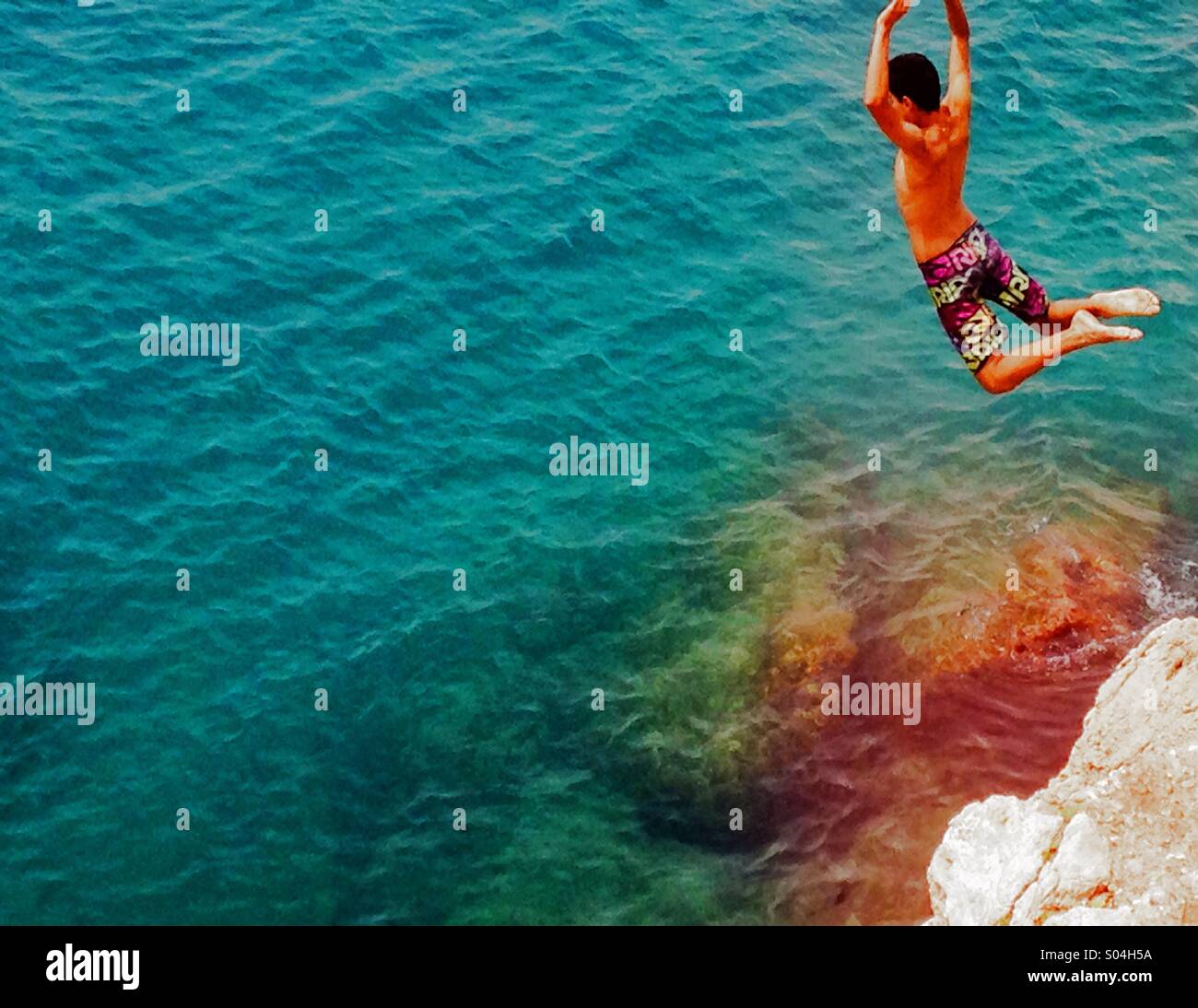 Ragazzo saltando da un dirupo nel mare Foto Stock