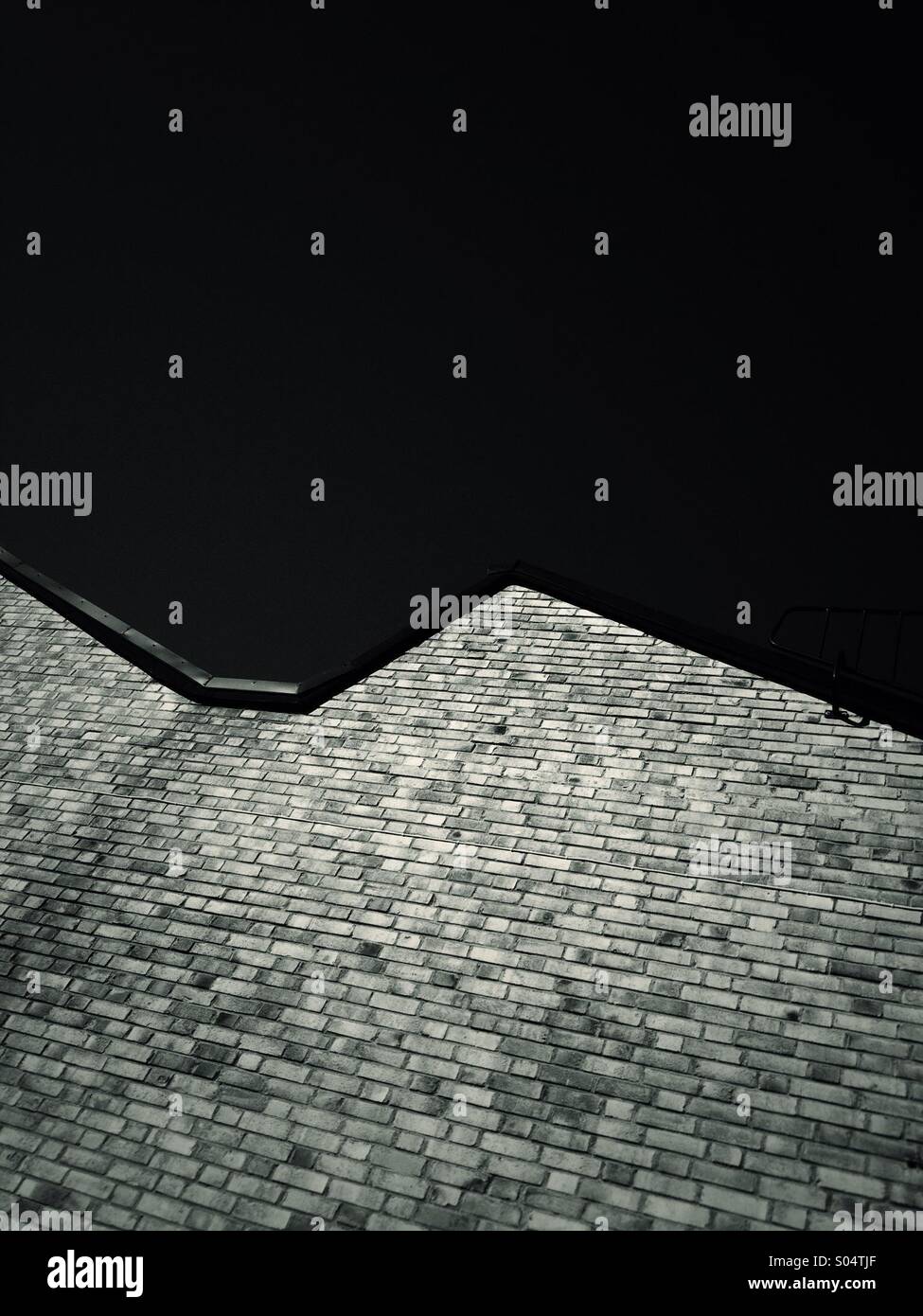 Muro di mattoni e tetto contro il cielo scuro. Foto Stock