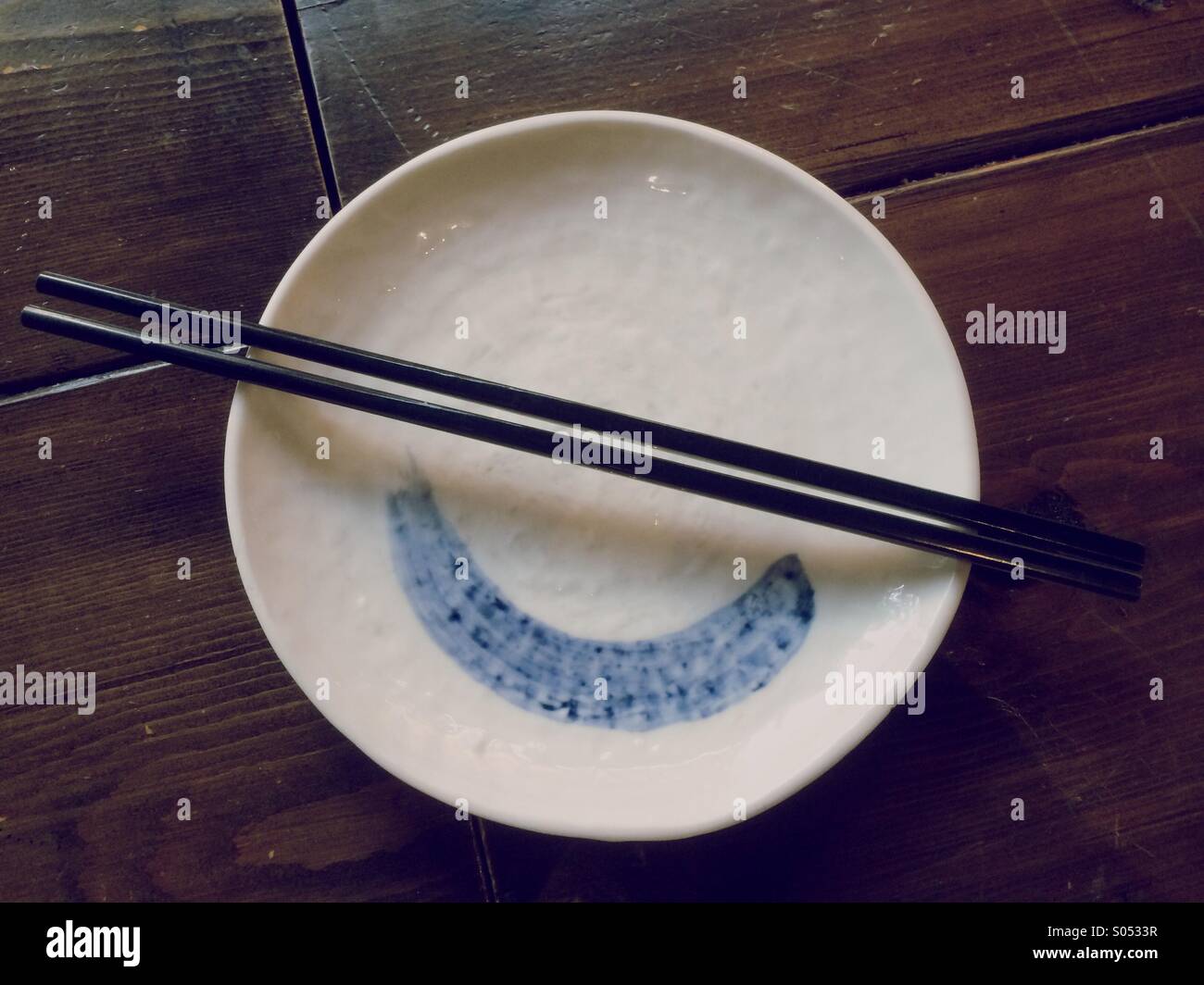 Nero bacchette di legno appoggiata su un vuoto piastra bianca in un ristorante asiatico. - Immagine stock catturata con smartphone