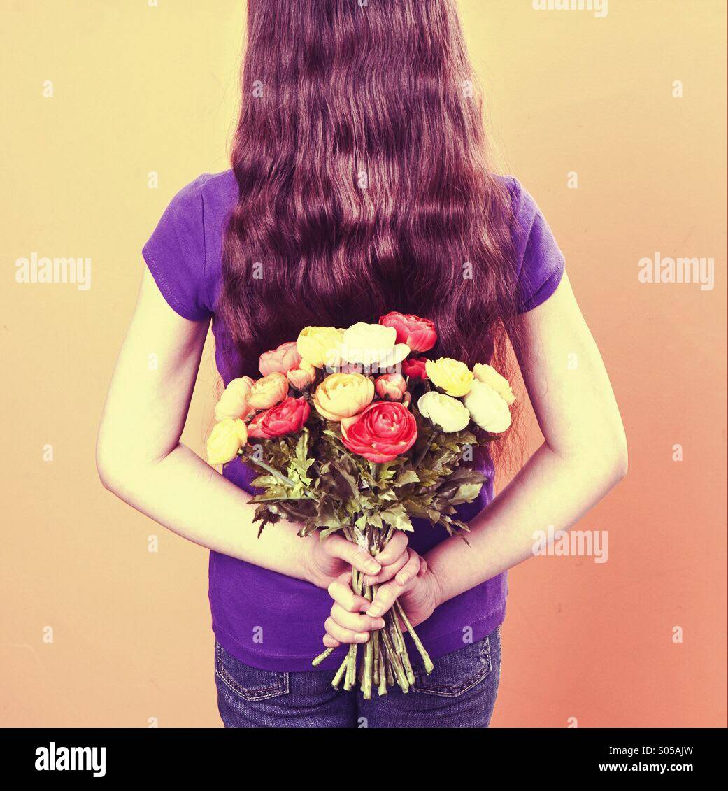 Ragazza giovane trattiene i fiori dietro la schiena Foto Stock