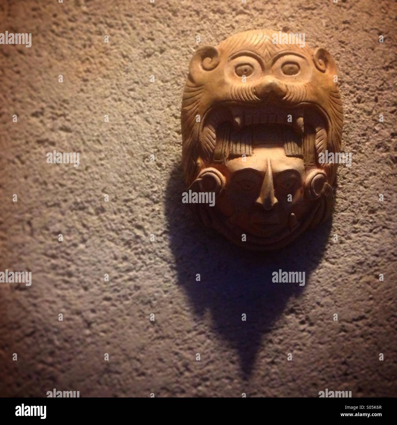 Una scultura in legno di un uomo che indossa una maschera di jaguar decora una parete in Flycatcher Inn a Santa Elena, Yucatan, Messico - Immagine stock catturata con smartphone