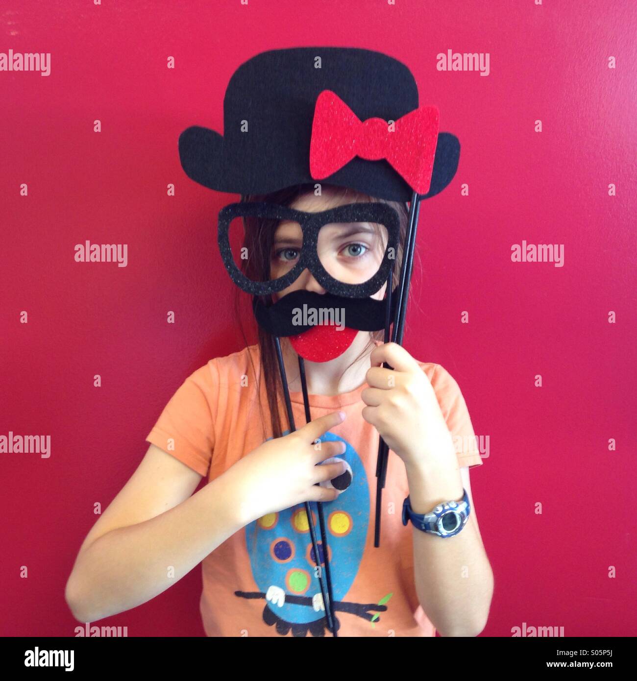 Silly kid indossa occhiali finti e un baffi contro un muro rosso. Foto Stock