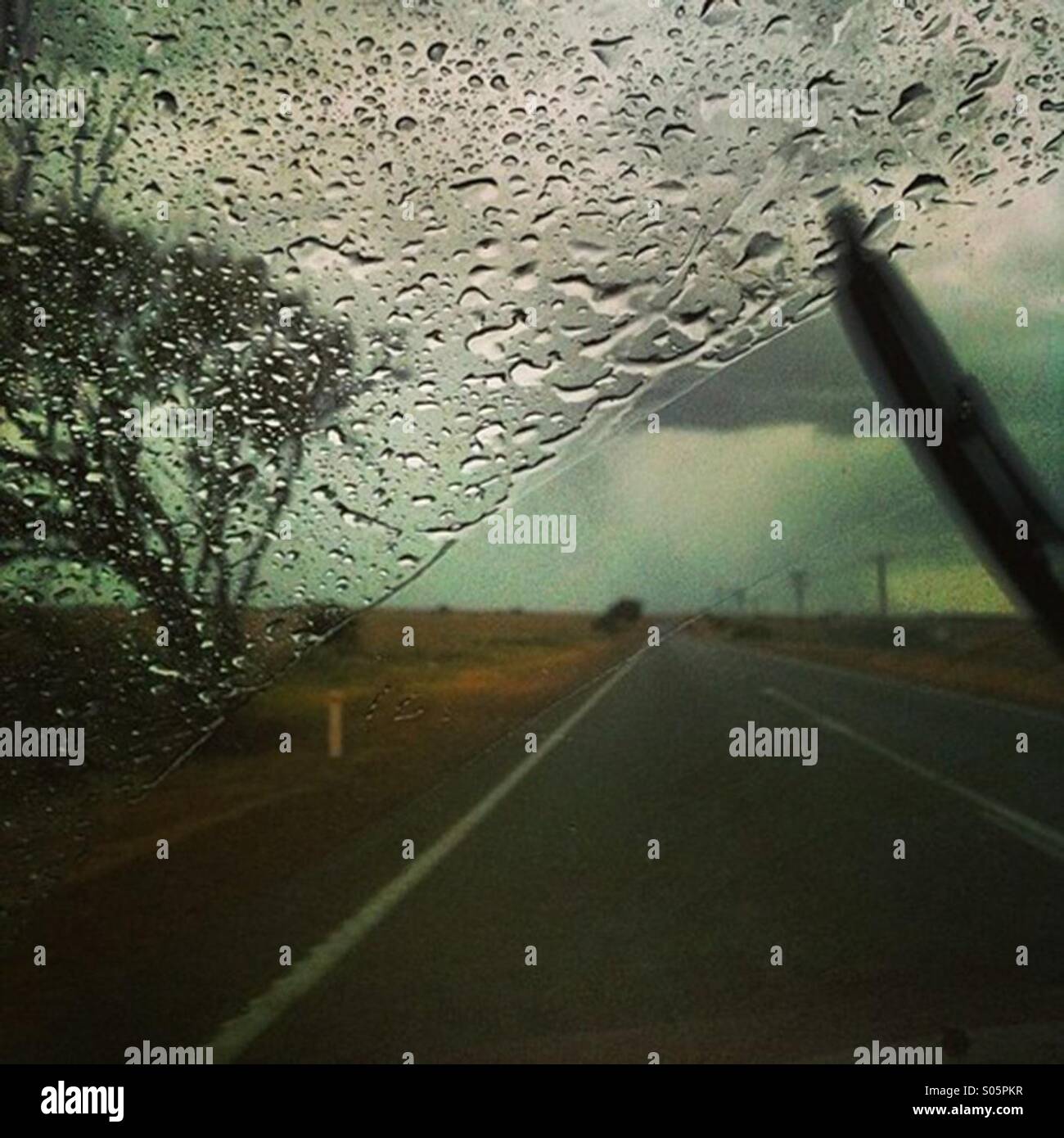 La pioggia su di un parabrezza di automobile durante la guida lungo un outback road in Australia Foto Stock