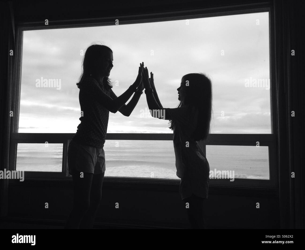 Due ragazze in silhouette alta cinque di fronte a una finestra immagine. L'immagine è in bianco e nero Foto Stock