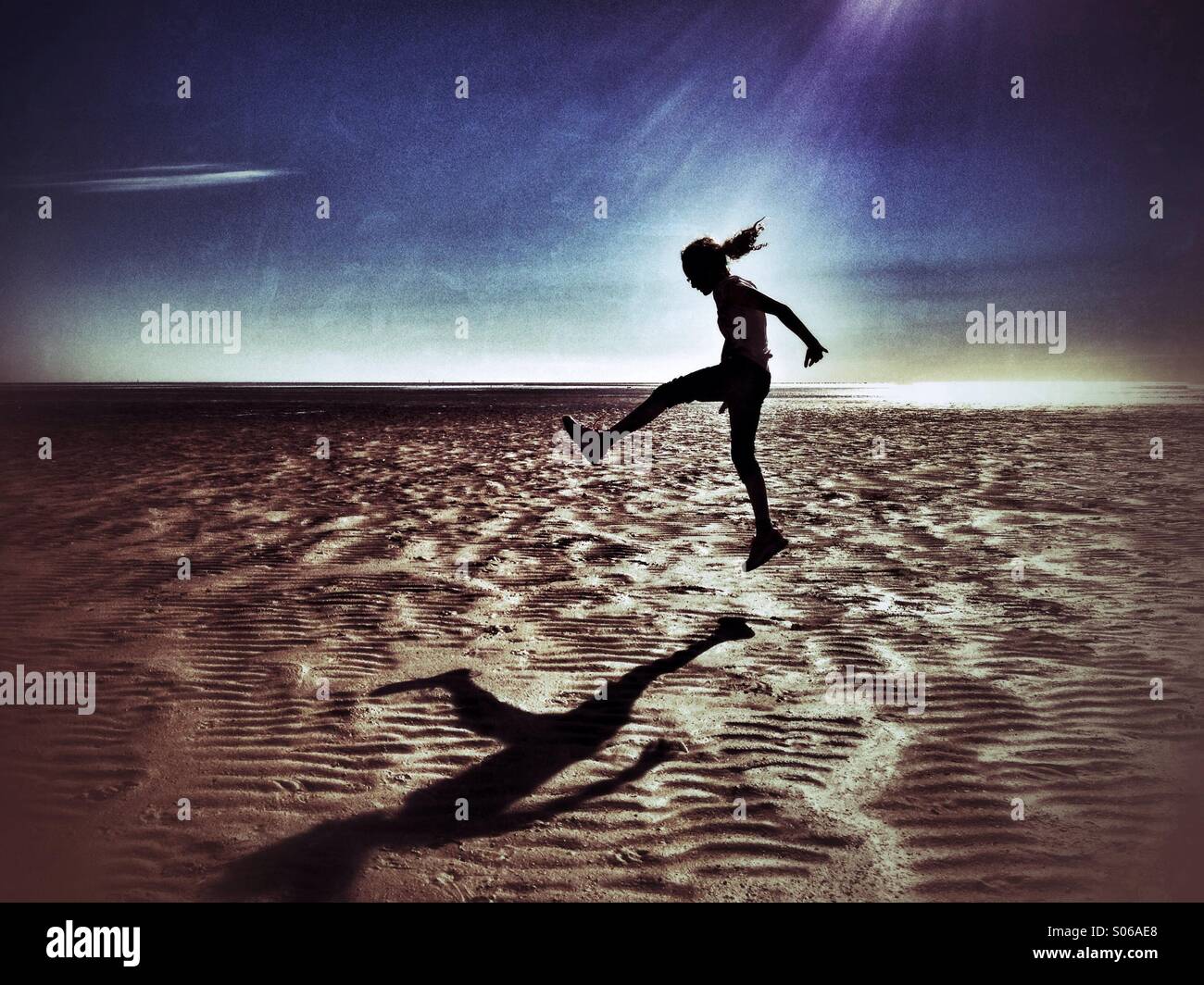 Ragazza salto sulla spiaggia vuota in silhouette Foto Stock