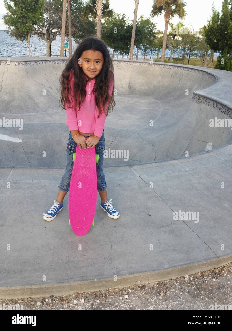 Una bambina di sette anni con il suo skateboard rosa in un parco della città in Florida. Foto Stock