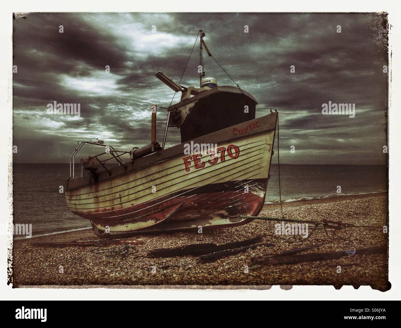Nave da pesca sulla spiaggia di ciottoli nel Kent, Inghilterra. Dark nuvole temporalesche si muovono velocemente su un mare calmo. Credito foto - © COLIN HOSKINS. - Immagine stock catturata con smartphone