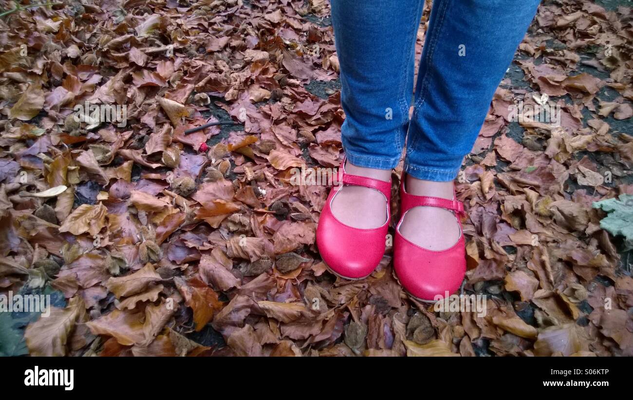 La ragazza di smart red shoes in piedi in foglie di autunno. Foto Stock