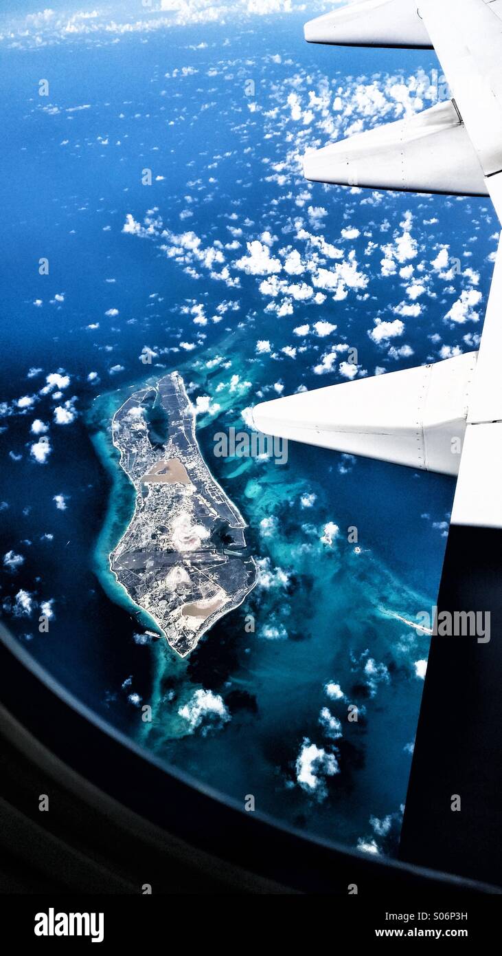 Un isola dei Caraibi visto attraverso la finestra di un aereo, che mostra una parte dell'ala bianca e puffy nuvole. - Immagine stock catturata con smartphone