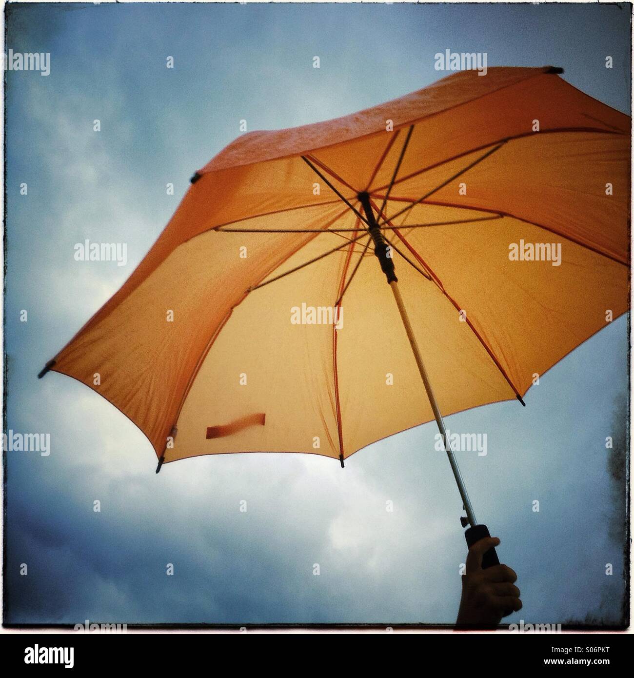 Aprire ombrello arancione isolato su sfondo con cielo nuvoloso Foto Stock