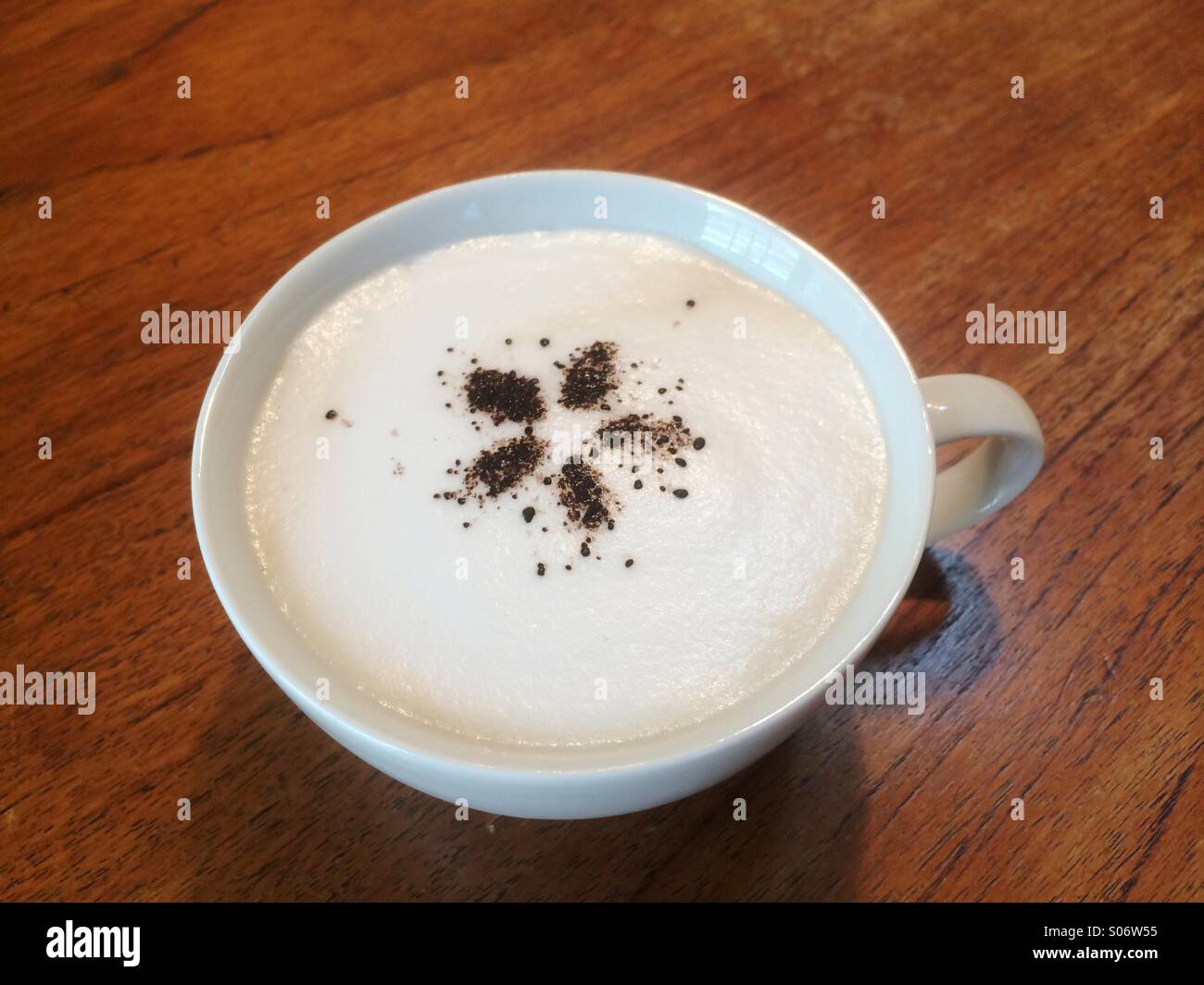 Caffè Latte cosparso di cacao e con un disegno di fiori nel centro. Foto Stock