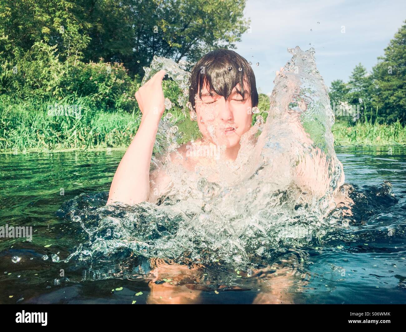 Ragazzo gli spruzzi di acqua sul suo volto in un fiume puro Foto Stock