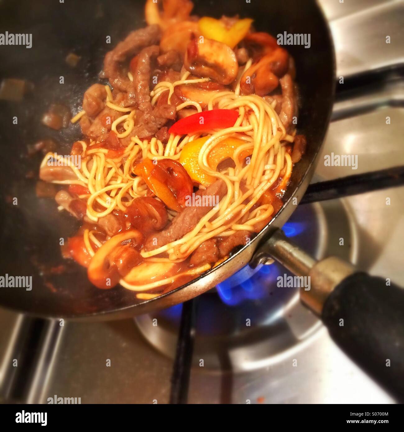 La cottura di un piatto di cucina orientale di carni bovine Chow Mein sopra una fiamma a gas in un wok Foto Stock