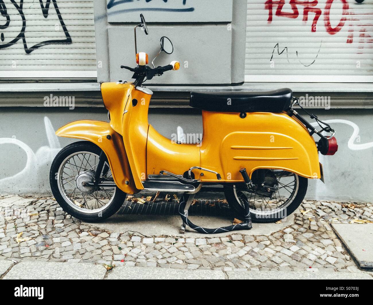 Vecchio motorino giallo scooter parcheggiato sulla strada di Berlino nella parte anteriore della parete graffitied Foto Stock