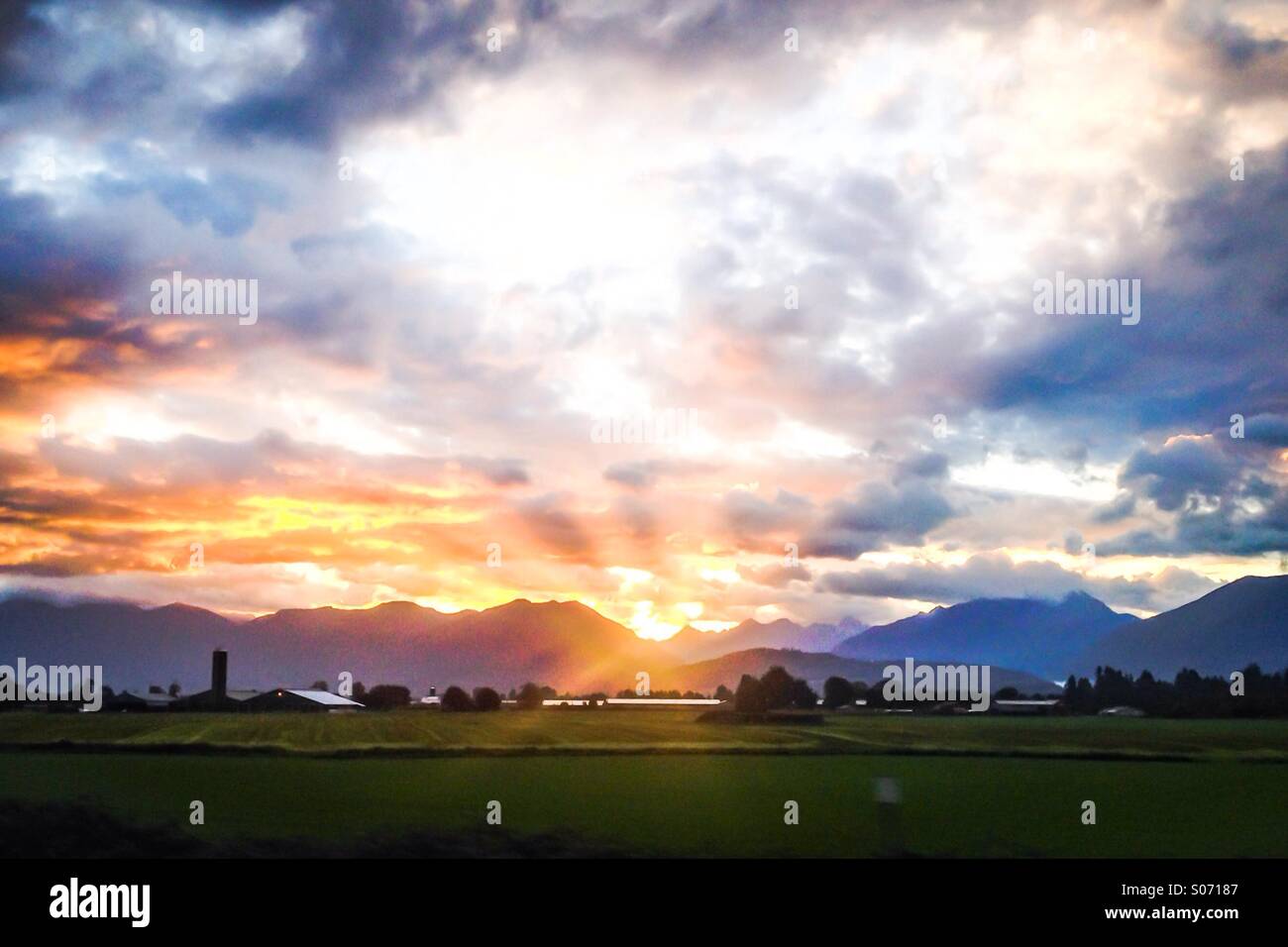 Il sorgere del sole tra le nuvole, sulle montagne. I verdi pascoli e la fattoria di ottenere le prime luci del giorno. - Immagine stock catturata con smartphone