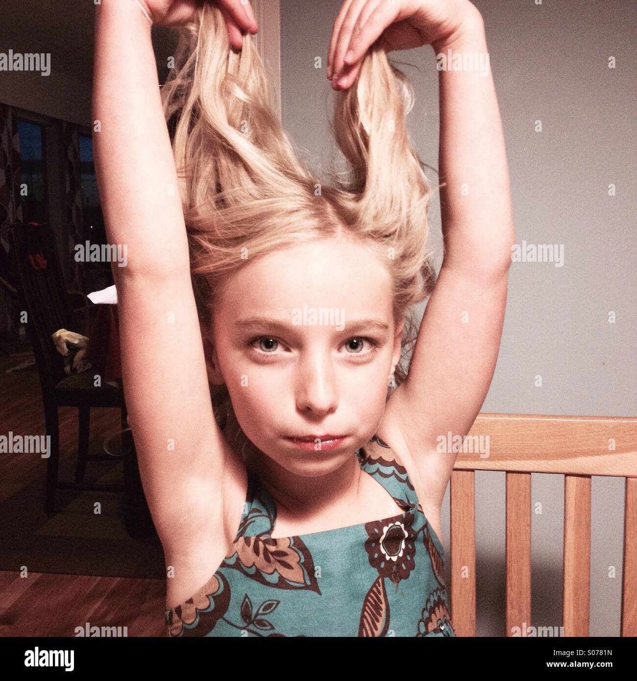 Un bambino di sei anni carina ragazza in un abito di partito a giocare con la sua lunga parentesi capelli biondi Foto Stock