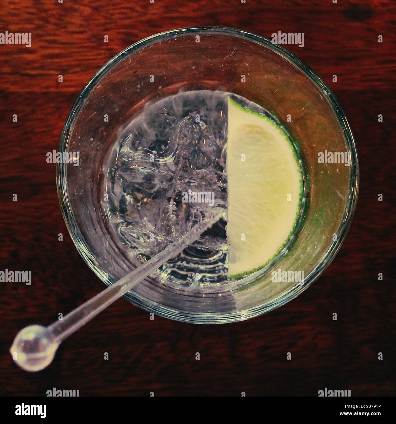 Vista dall'alto di un Gin e tonico con una sezione di lime e un bastone di swizzle su un tavolo di legno Foto Stock