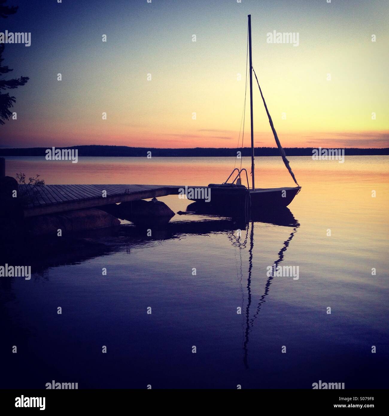 Una piccola barca a vela ormeggiata per la notte in un lago finlandese in Artico il sole di mezzanotte - Immagine stock catturata con smartphone