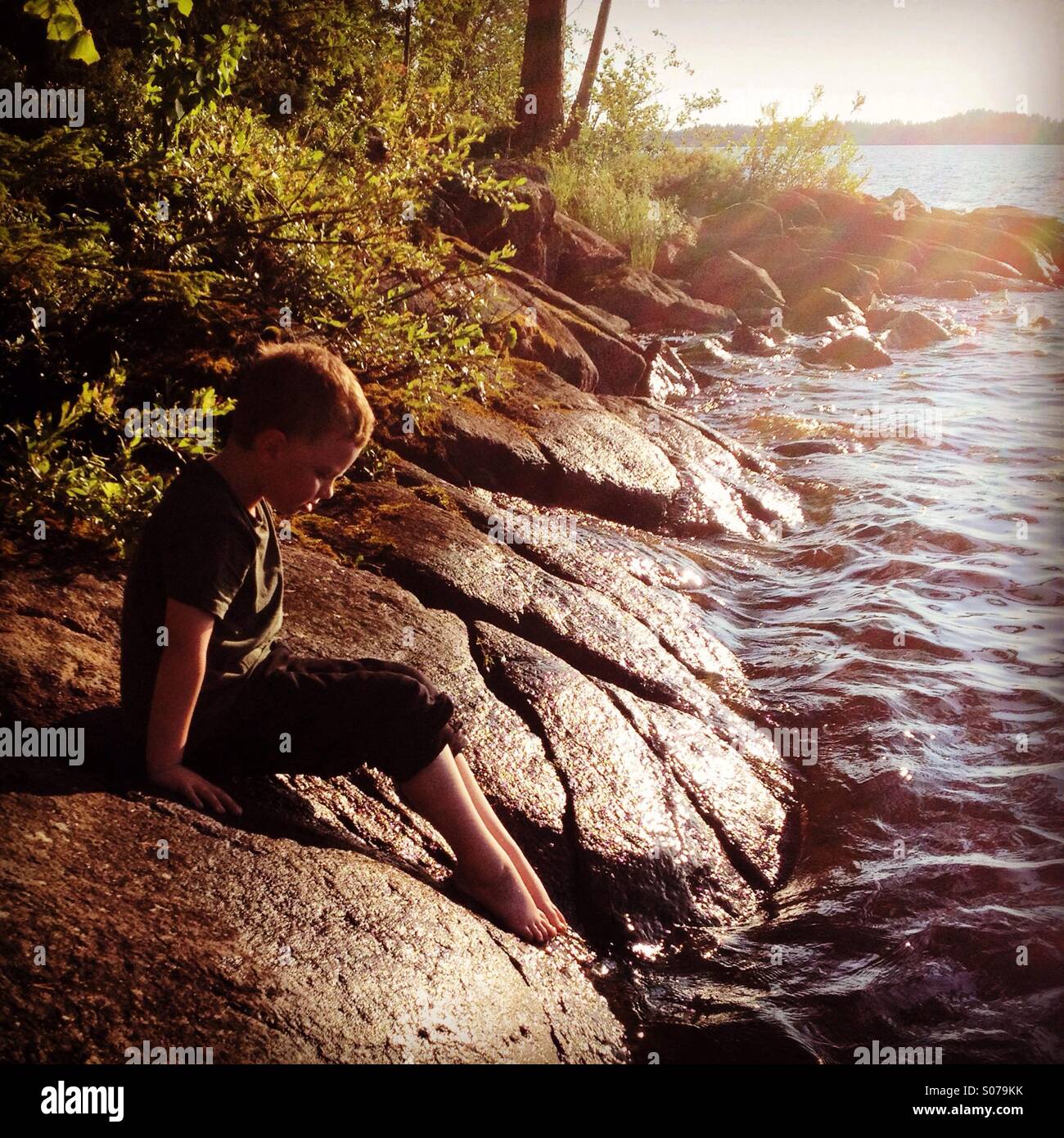 Un giovane ragazzo immergendo le sue dita dei piedi in acqua in un paese nordico summerhouse scandinavo lago Foto Stock