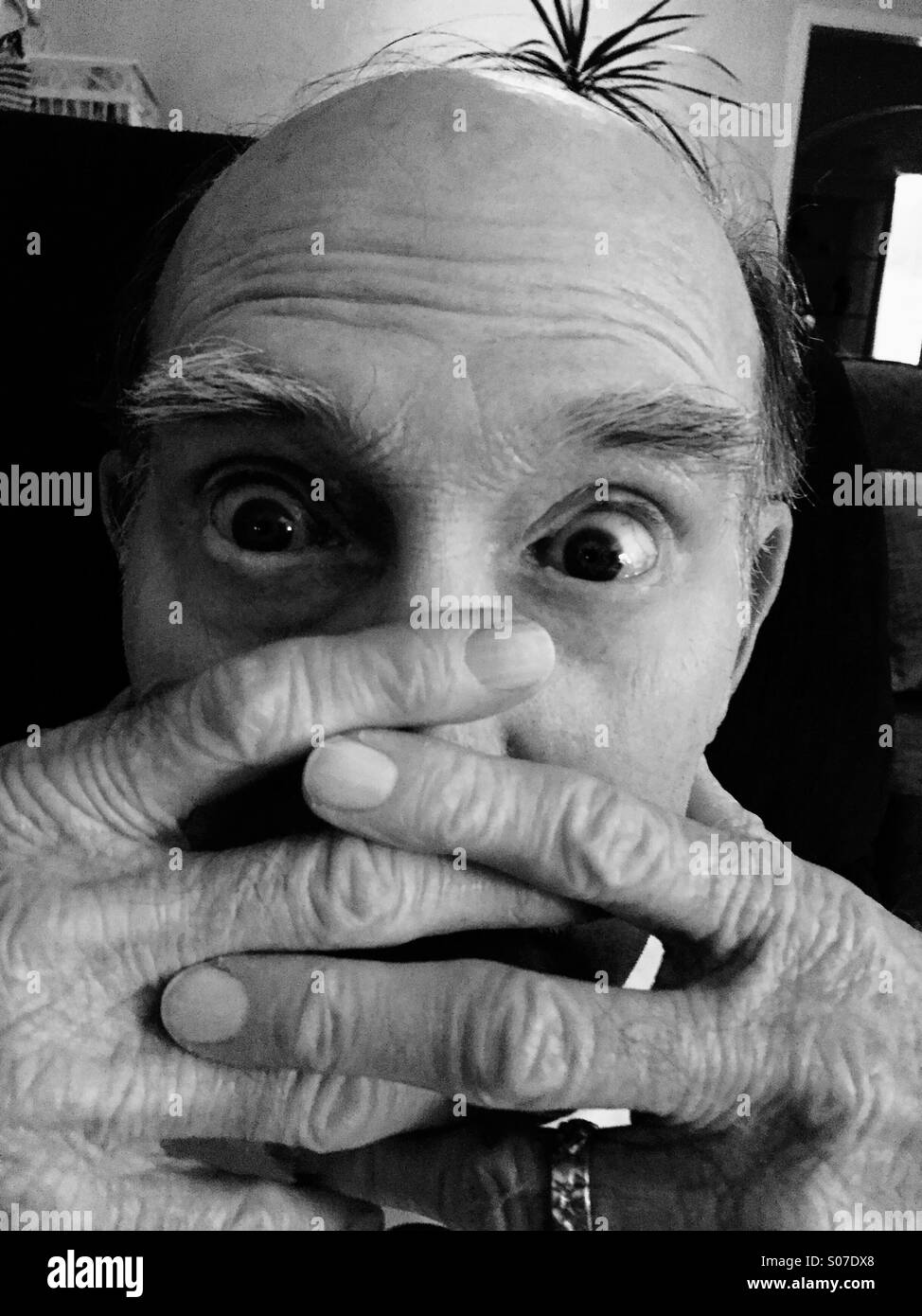 Un vecchio uomo caucasico con occhi spalancati lacci le sue dita sulla sua faccia inferiore. - Immagine stock catturata con smartphone