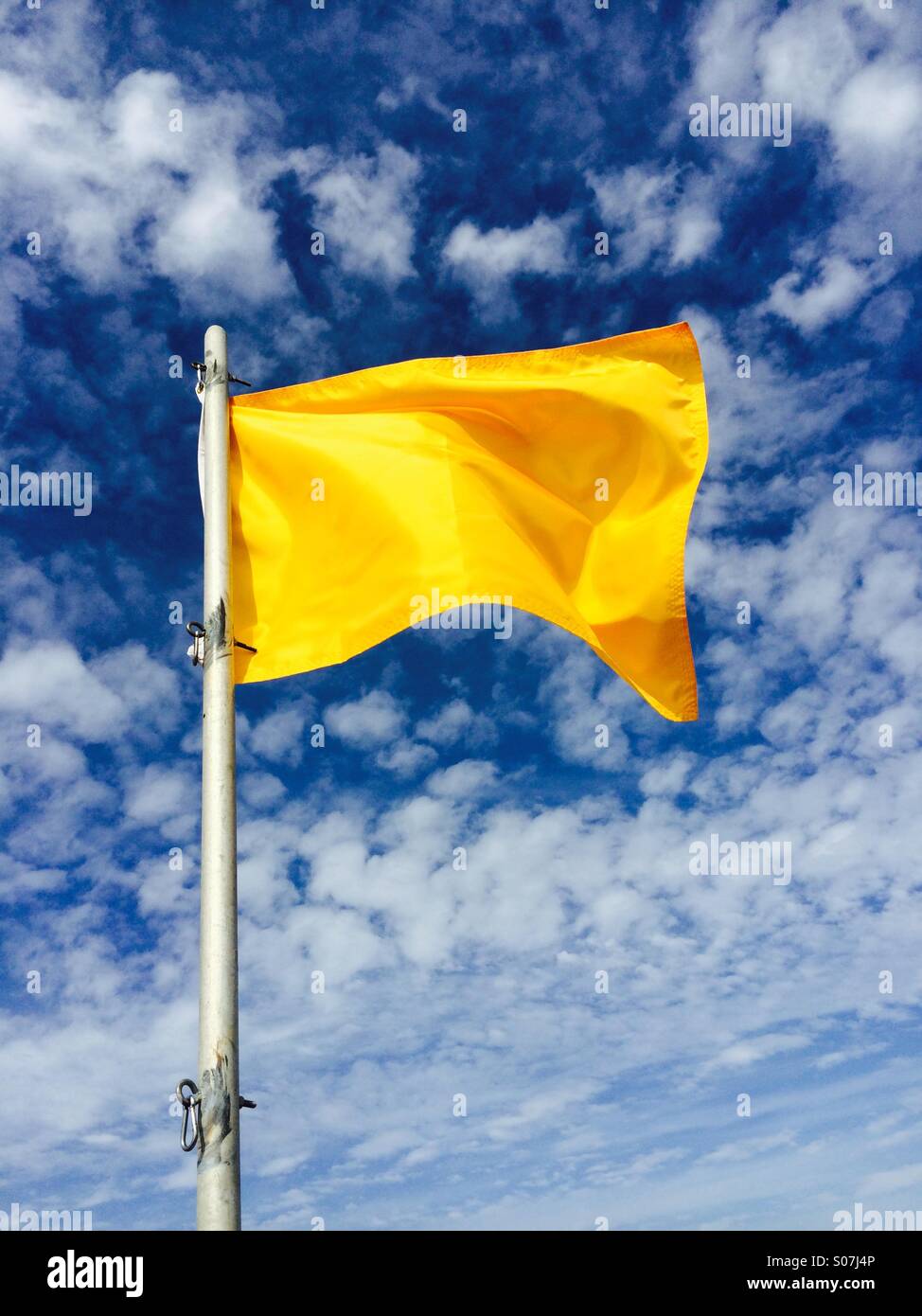 Un giallo di avvertimento sulla spiaggia bandiera contro il cielo blu. Foto Stock