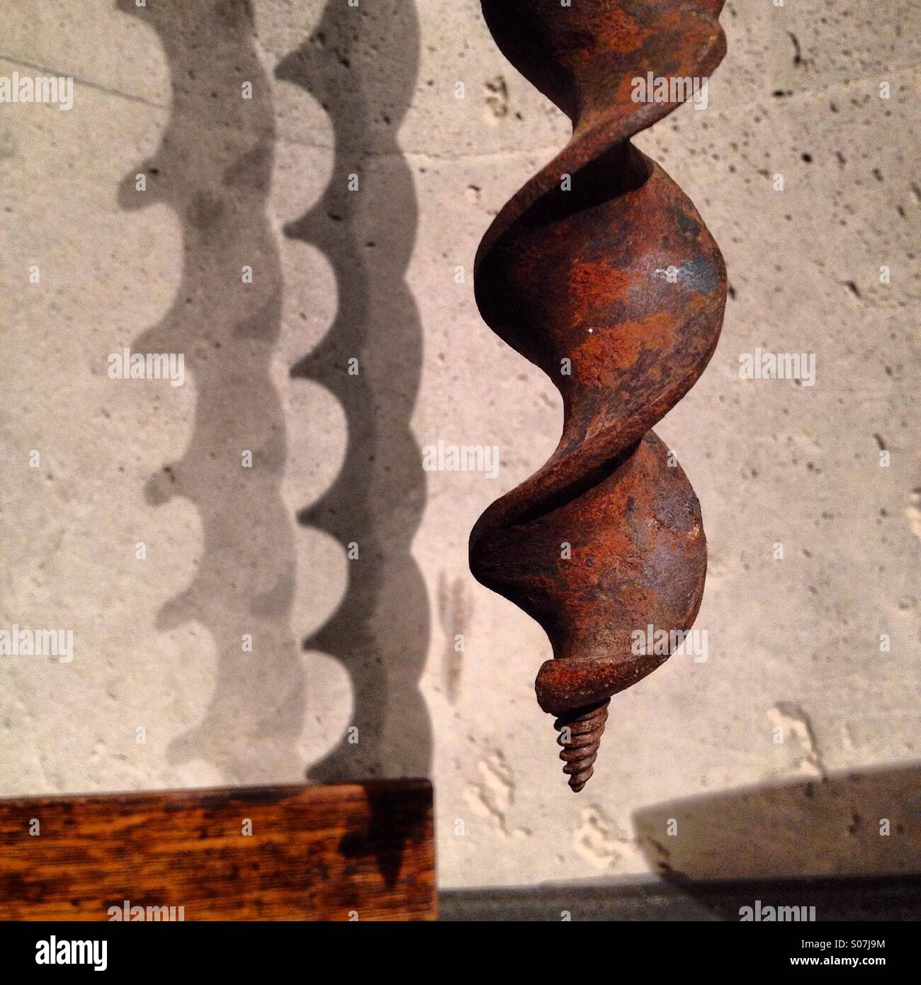 Un vecchio arrugginito trivella appesi al muro in un workshop che gettano ombre Foto Stock