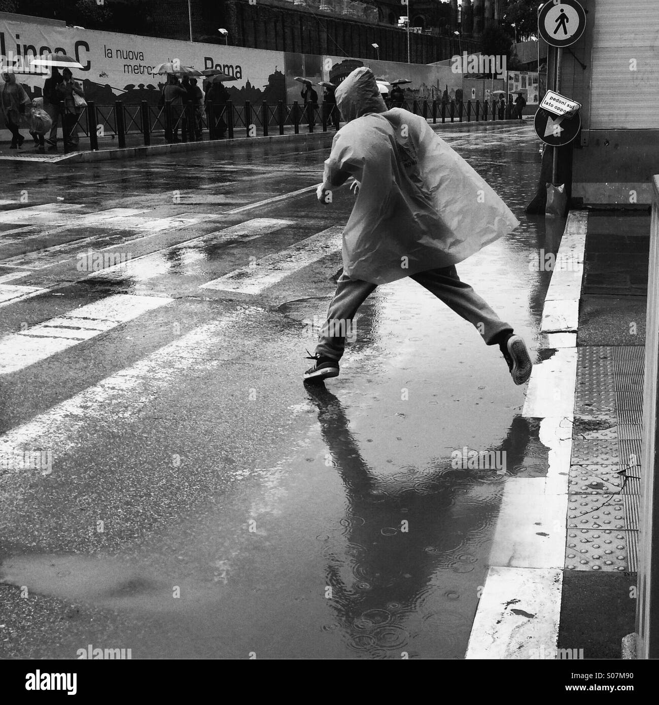 Un ragazzo salta su una pozzanghera in strada Foto Stock