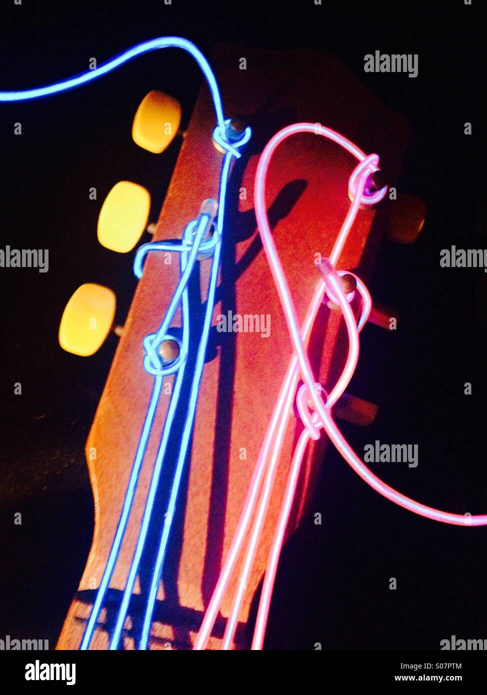 La testa di una chitarra acustica con le sue stringhe sostituito con electro filo luminescente Foto Stock