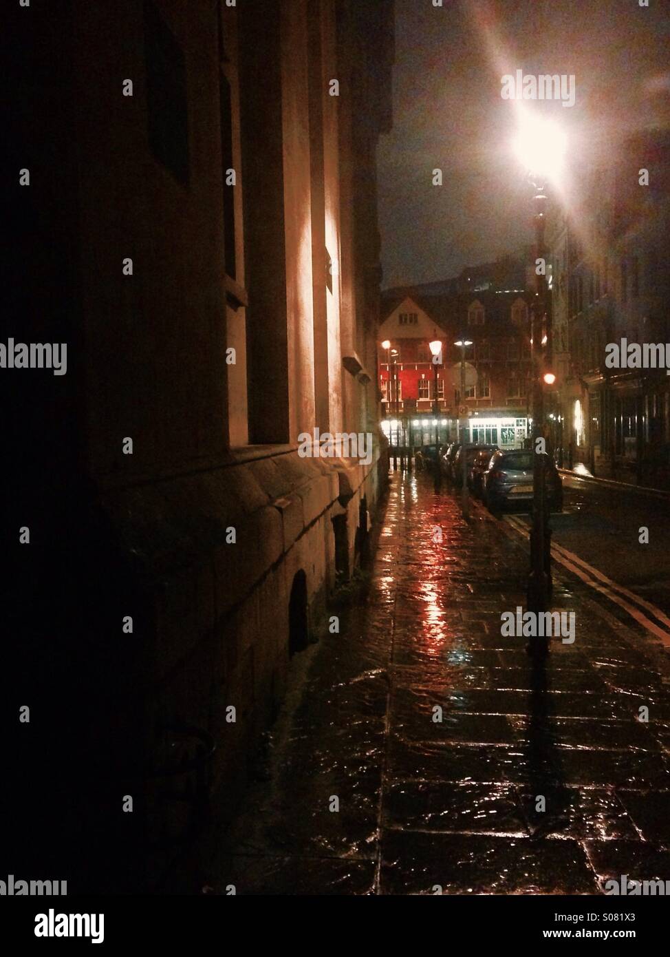 Il buio strade bagnate di Spitalfields con qualche illuminazione su la parete della chiesa e il vecchio mercato rosso in background in una fredda notte tranquilla per strada-luce. Foto Stock