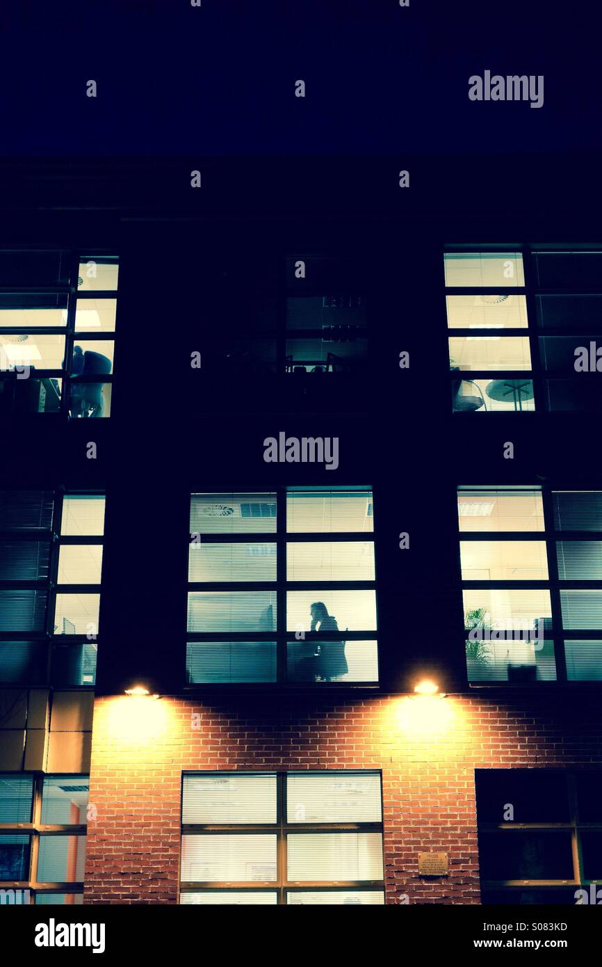 Lavora fino a tardi ancora - blocco di ufficio di notte con silhouette Foto Stock