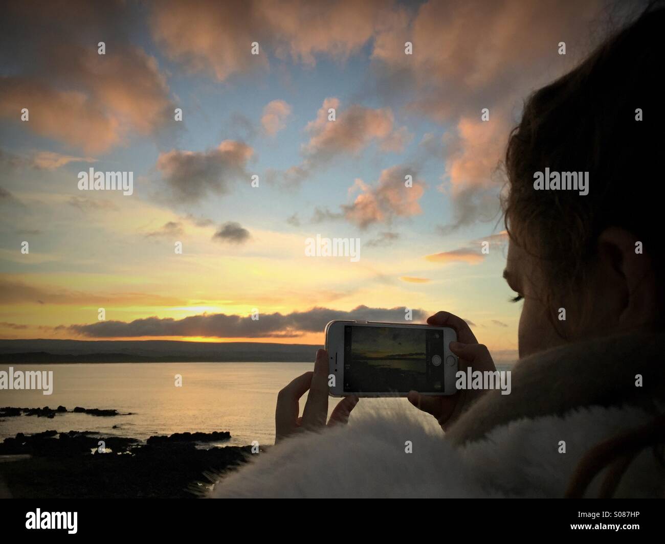 Giovane donna utilizzando iPhone per scattare foto di bel tramonto Foto Stock