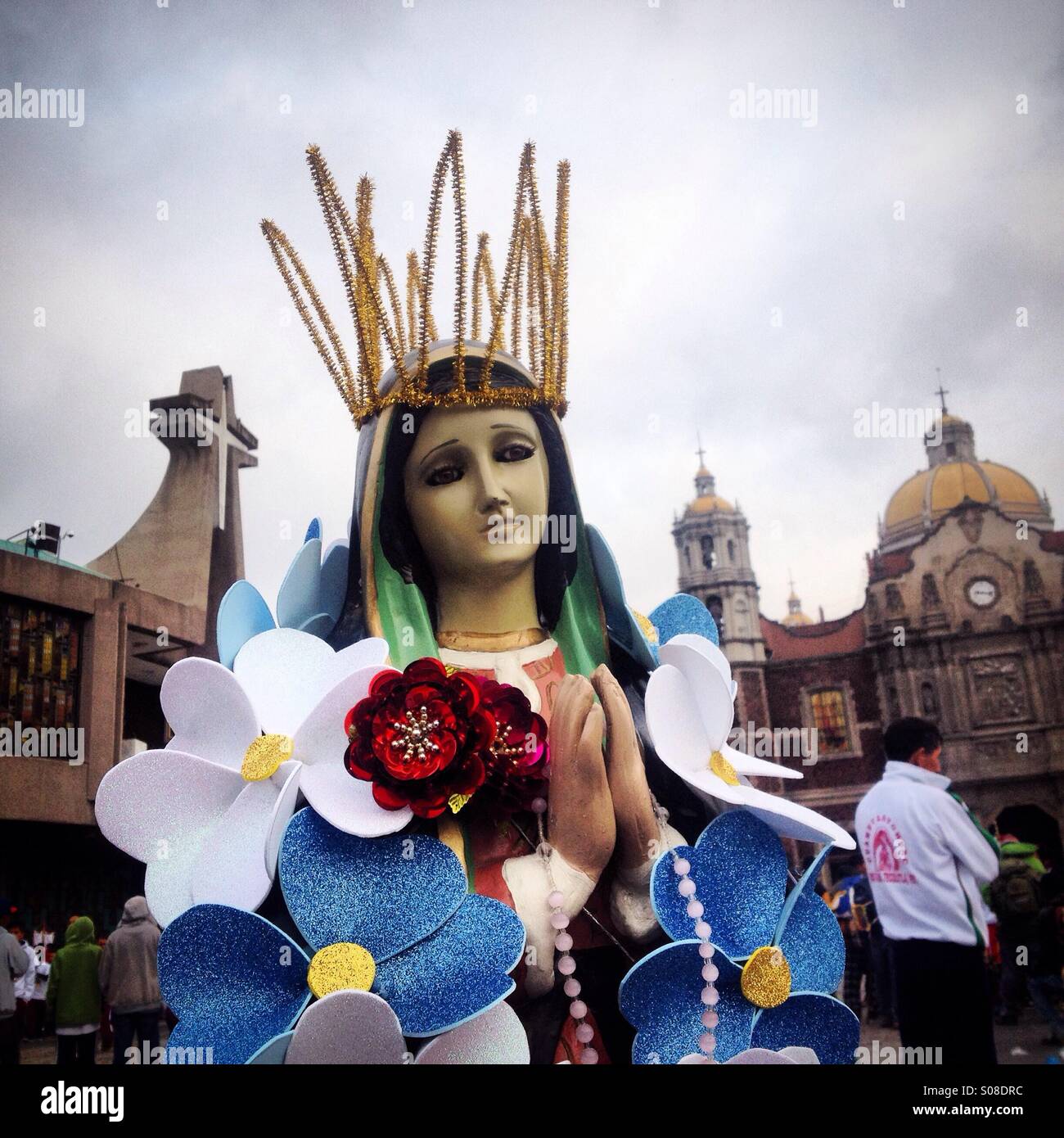 Una immagine della Vergine di Guadalupe decorate con fiori di plastica sorge sul terreno durante il pellegrinaggio alla Basilica di Nostra Signora di Guadalupe Tepeyac Hill, Città del Messico, Messico - Immagine stock catturata con smartphone