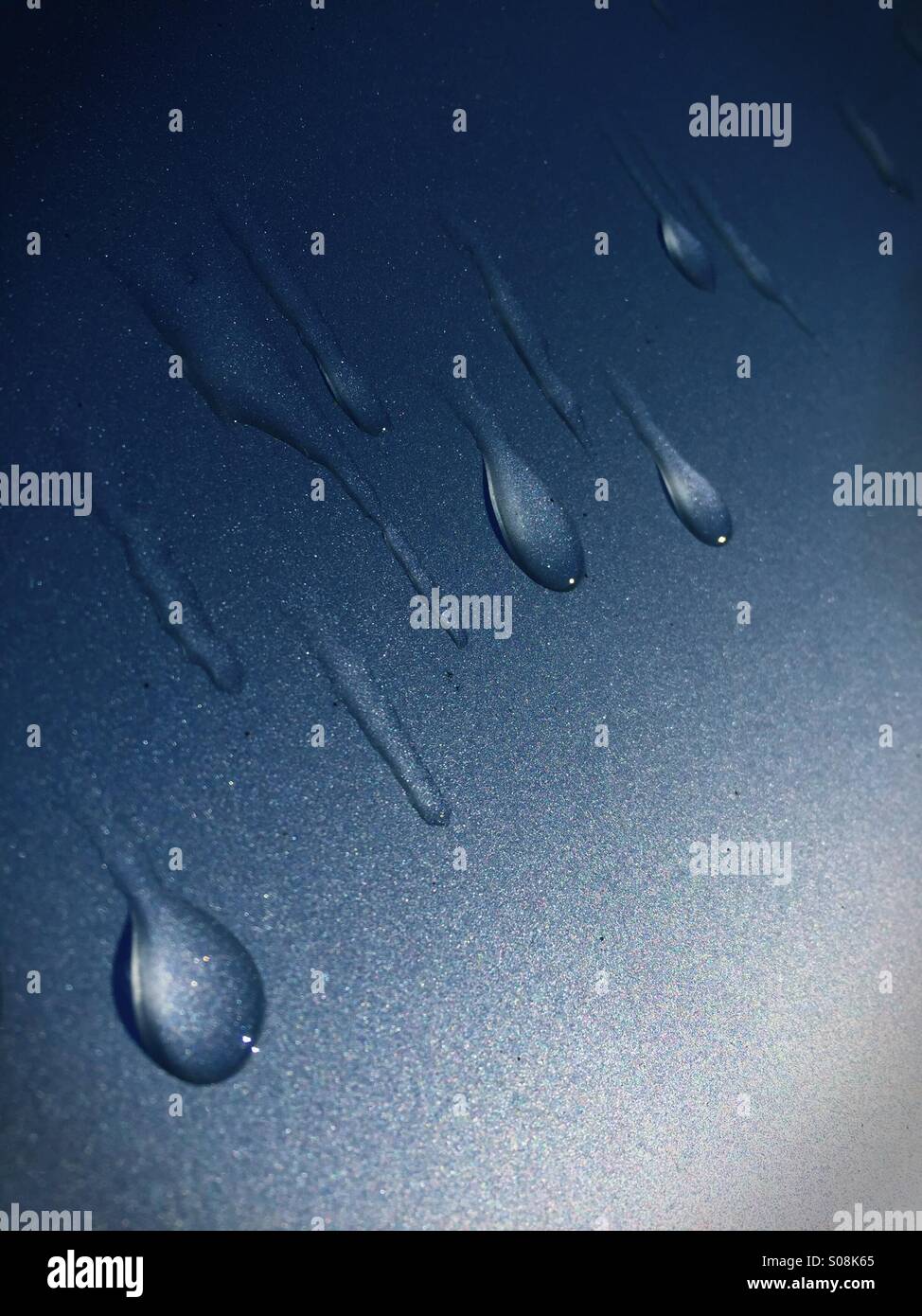 Gocce d'acqua eseguiti su un blu superficie metallica Foto Stock