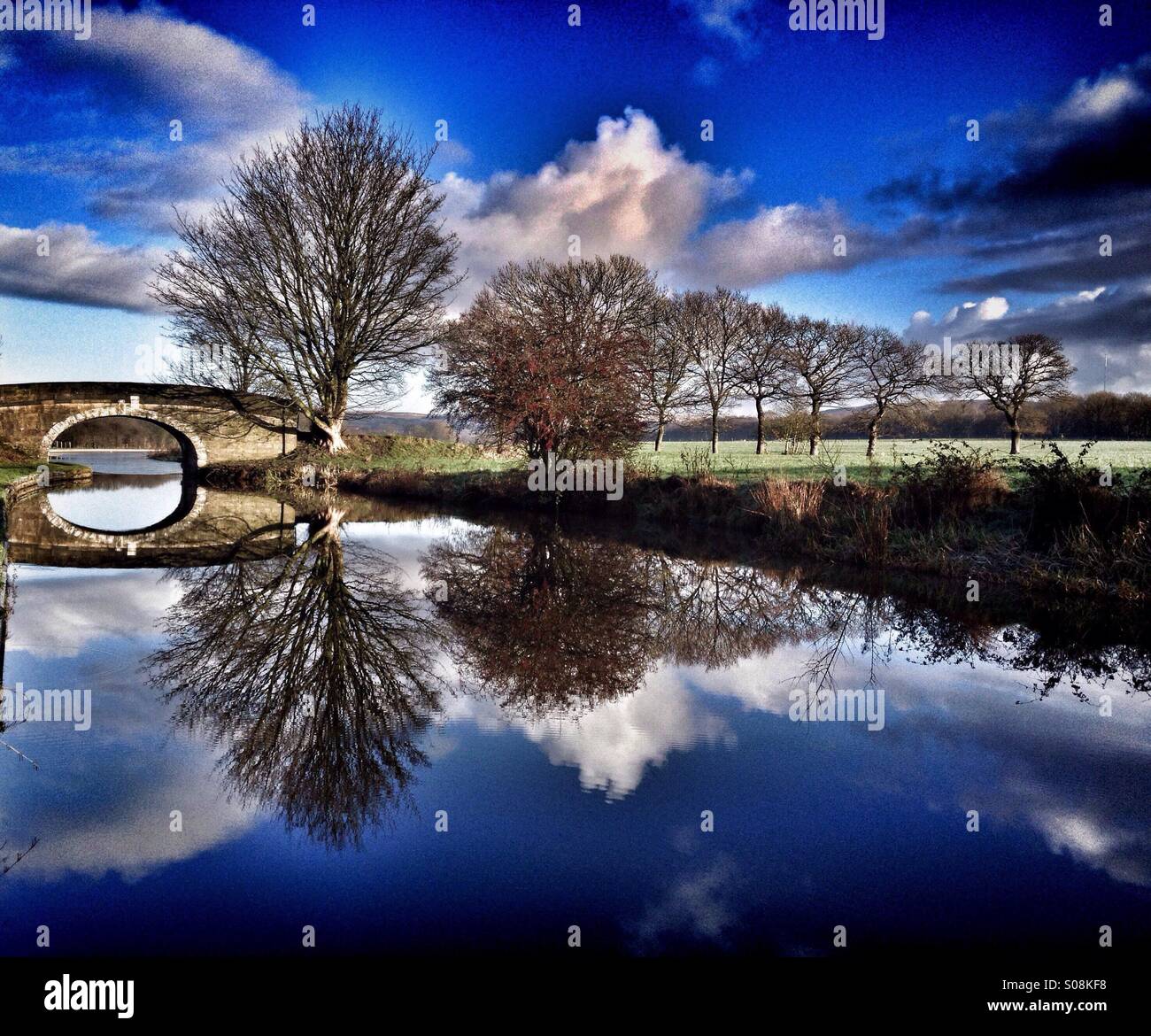 Il ponte di pietra e alberi specchio riflettente immagine nel canale Foto Stock