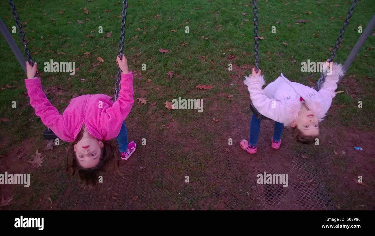 Le ragazze giovani sorelle giocando sulle altalene al parco giochi. Foto Stock