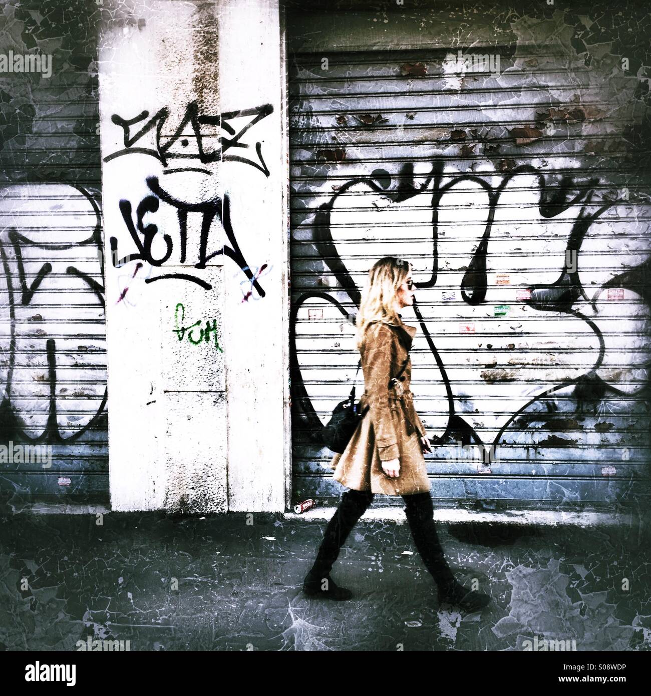 Giovane donna camminare passato alcune porte di garage e di un muro con graffiti su - Immagine stock catturata con smartphone