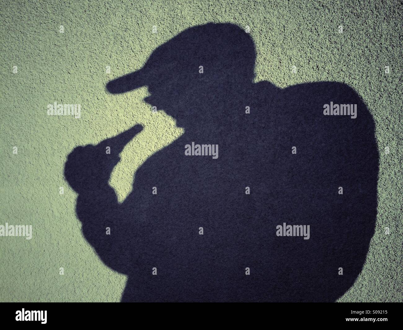 Ombra di un uomo che indossa un cappello da baseball di bere una bottiglia di sidro di mela - Immagine stock catturata con smartphone