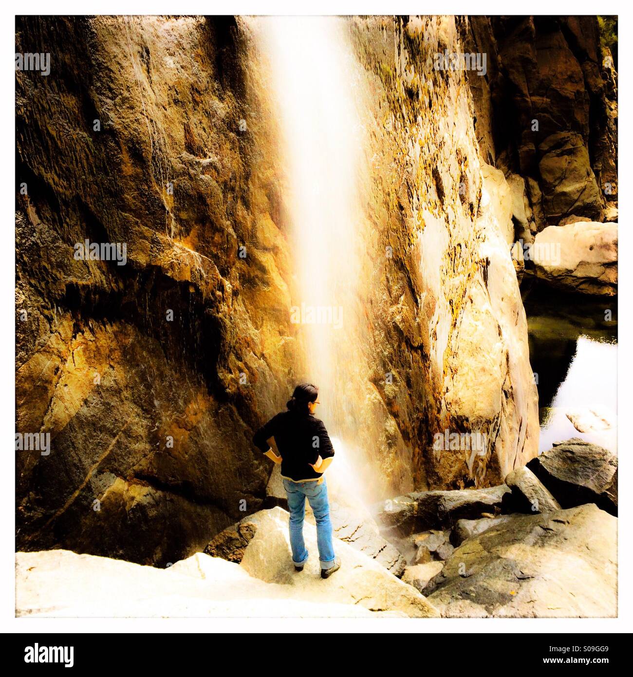 Una donna sta alla base inferiore di Yosemite Falls con un basso flusso di acqua durante la caduta. Il parco nazionale di Yosemite Valley, il Parco Nazionale di Yosemite, Mariposa County, California, Stati Uniti d'America Foto Stock