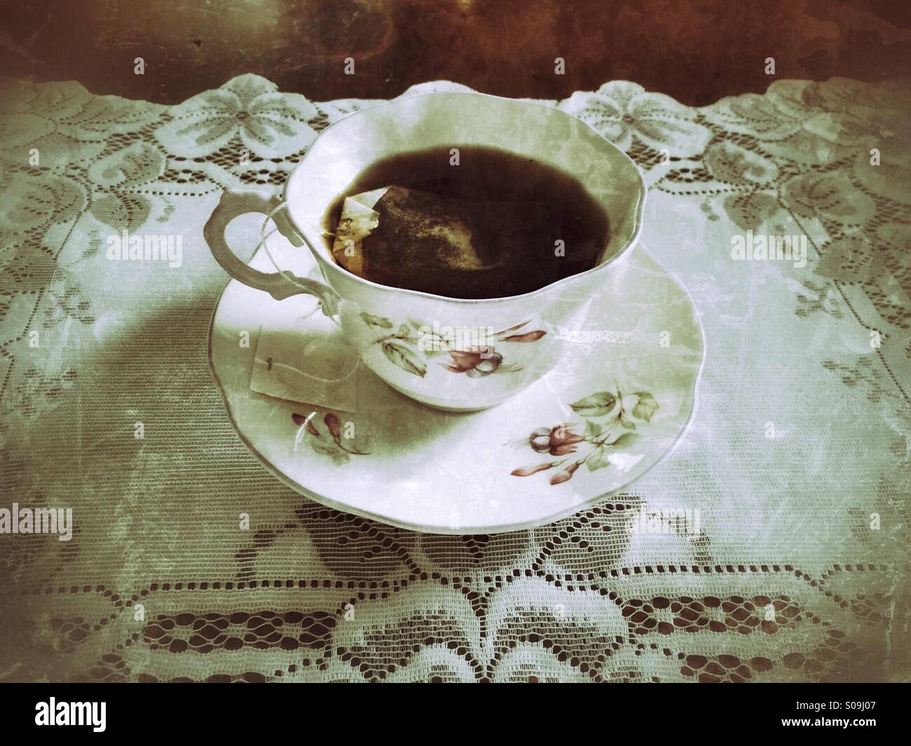 Una tazza di tè caldo in un vintage tazza e piattino con un sacchetto da tè, su un luogo di pizzo mat. Foto Stock