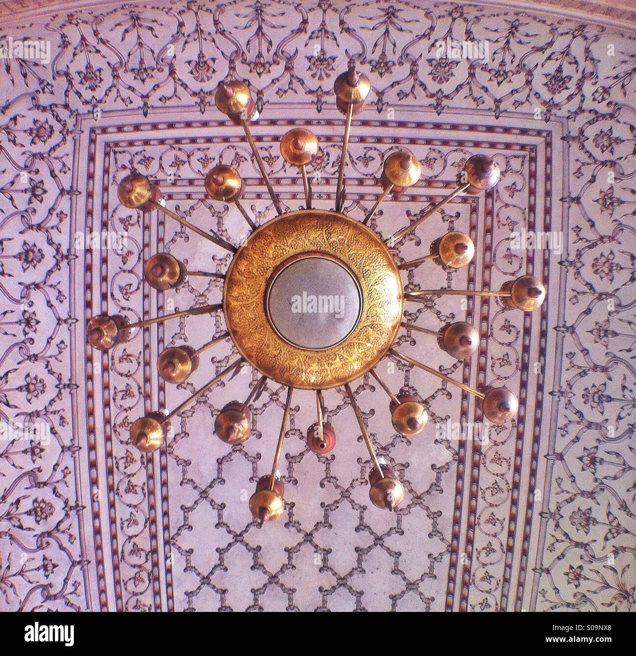 Un vecchio lampadario dorato appeso sulla sommità di una ornata architettura islamica. Foto Stock