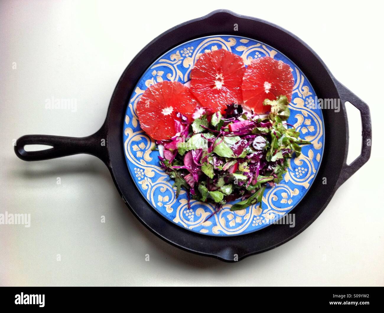 Insalata e pompelmo su un piatto decorativo su un ferro padella in ghisa - Immagine stock catturata con smartphone