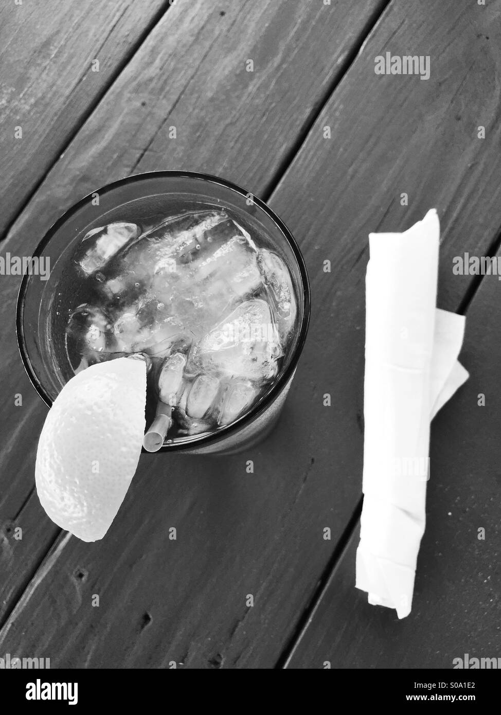 Bicchiere di acqua ghiacciata o limonata con un cuneo di limone su un tavolo da picnic in bianco e nero Foto Stock