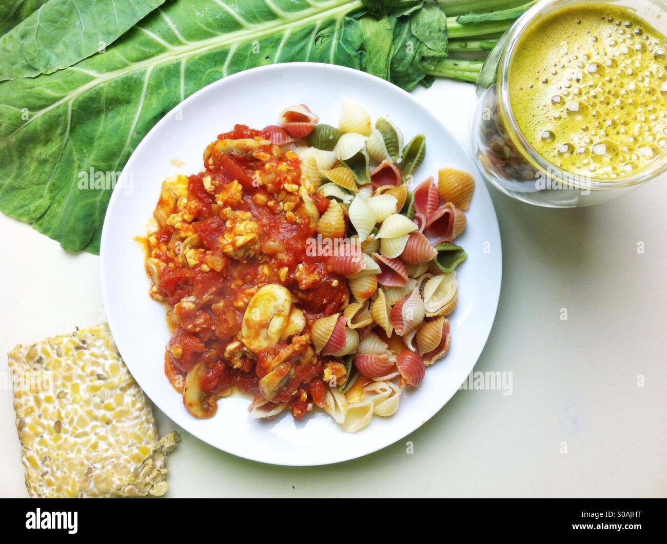 Pasto vegano di pasta e il tempeh con salsa di pomodoro fresco succo vegetale e una foglia di cavolo - Immagine stock catturata con smartphone